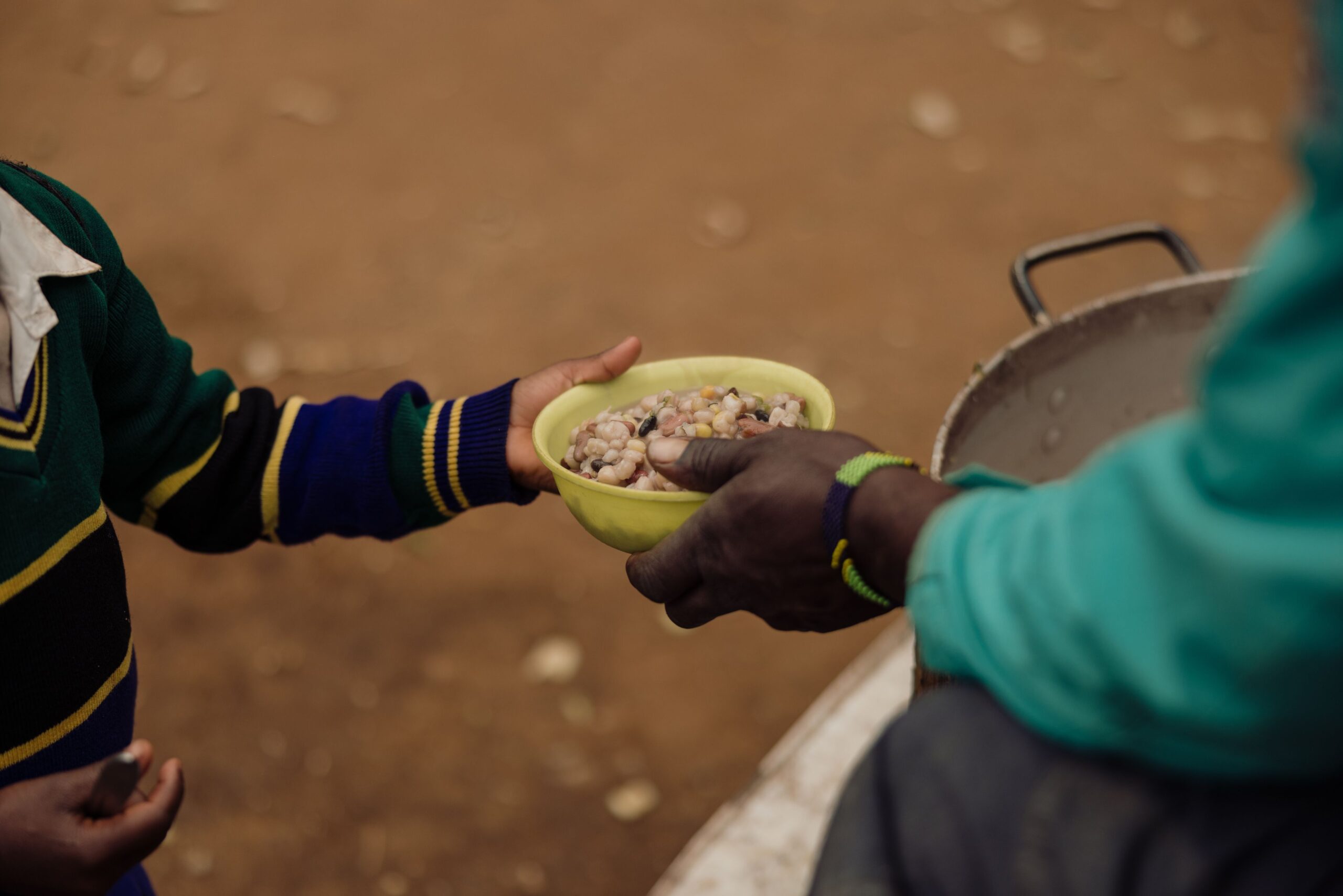 An outstretched adult hand places a bowl of food in a child’s hand.